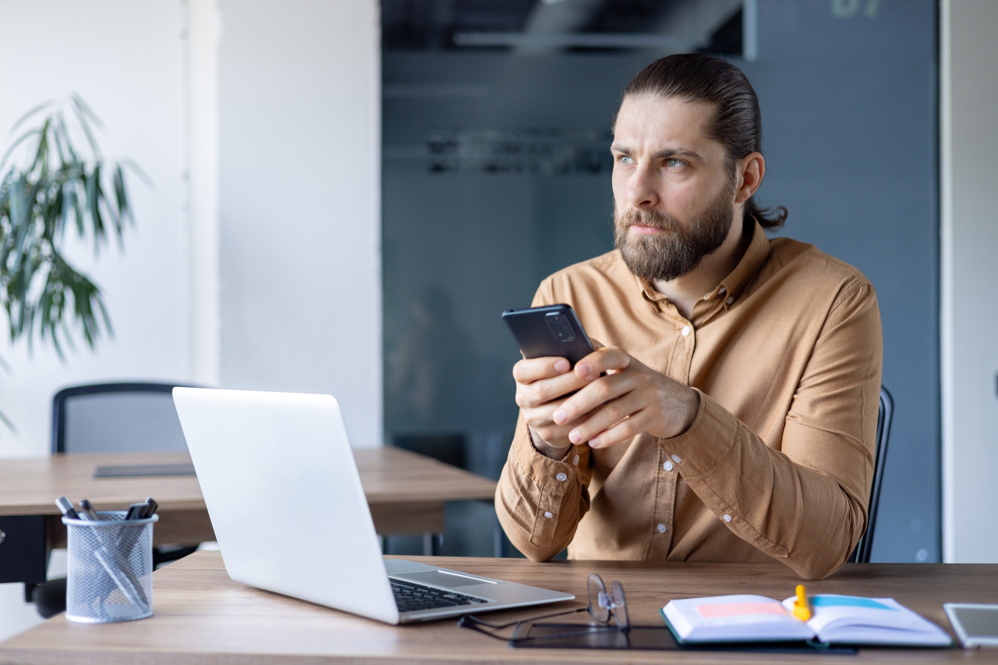 Business professional sitting at desk using smartphone and working on laptop