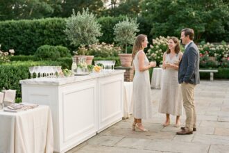 Cocktail chic en plein air sur terrasse avec mobilier de bar modulaire blanc et invités élégants conversant dans un cadre verdoyant