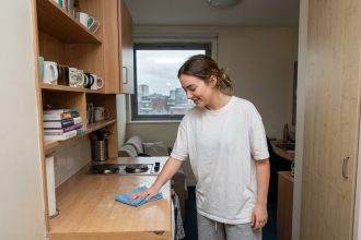 Jeune étudiante qui nettoie le plan de travail de sa kitchenette dans un studio compact et bien rangé